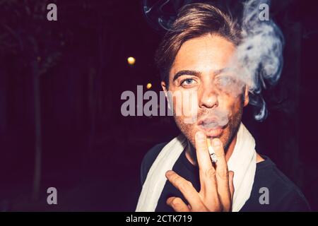 Close-up of handsome man smoking cigarette outdoors at night Stock Photo