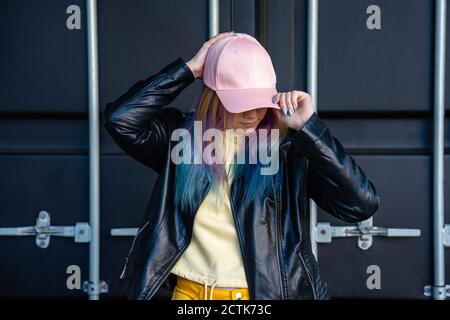 Portrait of young woman with dyed hair and baseball cap in front of black container Stock Photo