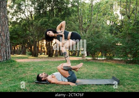 Man balancing girlfriend on legs while practicing acroyoga in public park Stock Photo