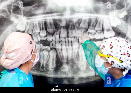 Dentist and assistant in protective workwear discussing about x-ray at office Stock Photo