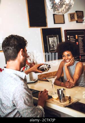 Smiling woman looking at male bartender preparing cocktail on bar counter Stock Photo