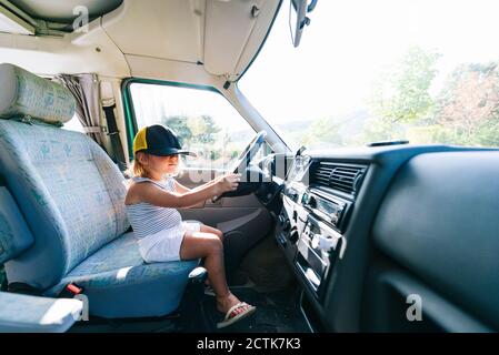 Girl wearing cap sitting on driver's seat in motor home Stock Photo