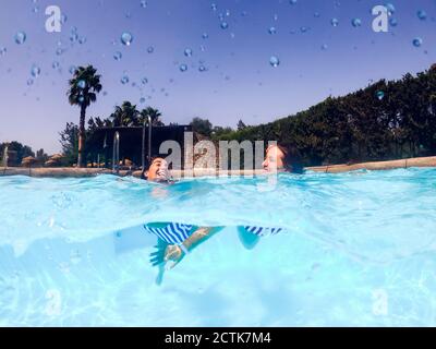 Happy female friends enjoying swimming in pool on sunny day Stock Photo