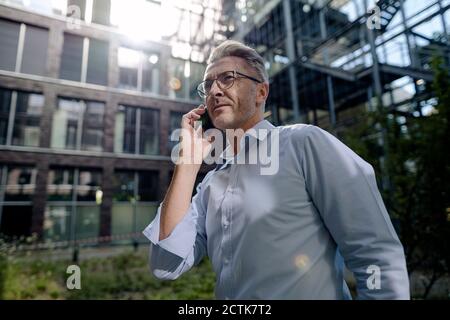 Male entrepreneur talking over smart phone while standing outside office building Stock Photo