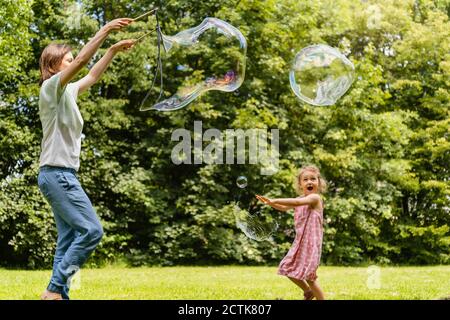 Happy daughter exploding bubble with mother at park Stock Photo