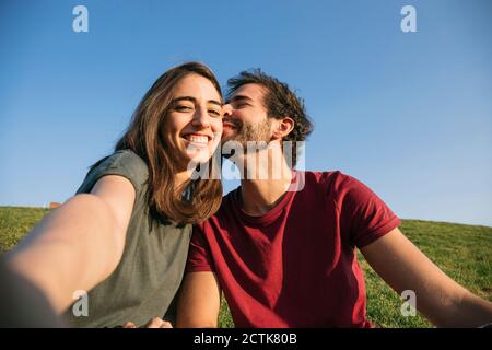 Woman taking selfie with man while sitting on grass Stock Photo