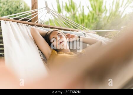 Young woman with arms raised sleeping on hammock in yard Stock Photo
