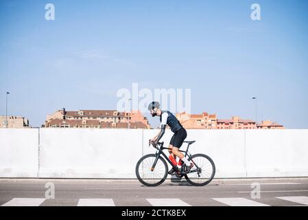 Male amputee cyclist riding bicycle on road against clear blue sky during sunny day Stock Photo