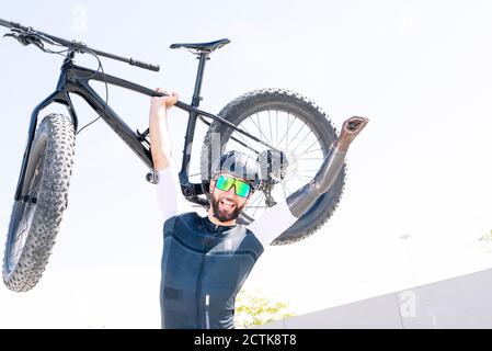 Cheerful male amputee athlete carrying bicycle while standing against clear sky Stock Photo