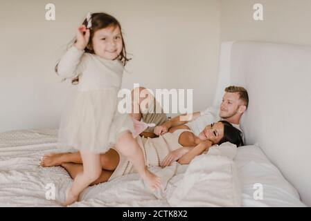 Playful daughter jumping on bed while parents lying in bedroom Stock Photo
