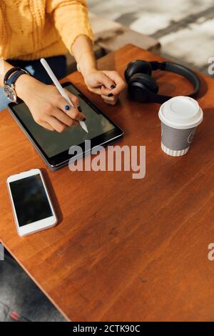 Midsection of young female student using digital tablet at sidewalk cafe table Stock Photo