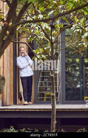 Bearded man talking over smart phone while standing at entrance of in tiny house Stock Photo
