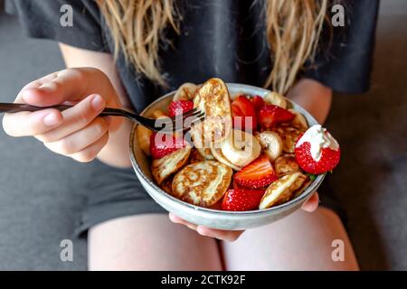 Mid section of teenage girl eating bowl of mini pancakes with strawberries and bananas Stock Photo