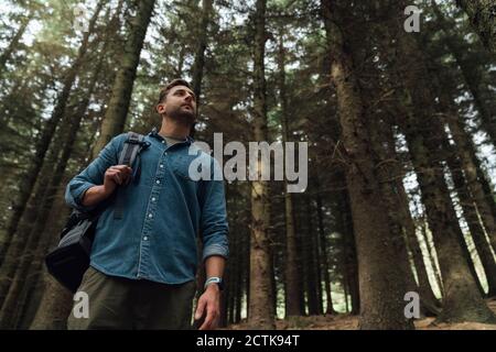 Mid adult man contemplating while standing against trees in forest
