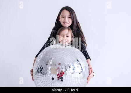 Sibling holding disco ball together in studio Stock Photo