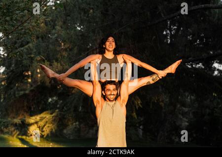 Smiling man lifting woman while practicing acroyoga in public park Stock Photo