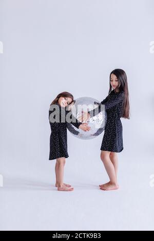 Sibling holding disco ball together while standing against white background in studio Stock Photo