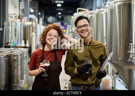 Portrait of happy man and woman holding clipboard and beer glass in craft brewery Stock Photo