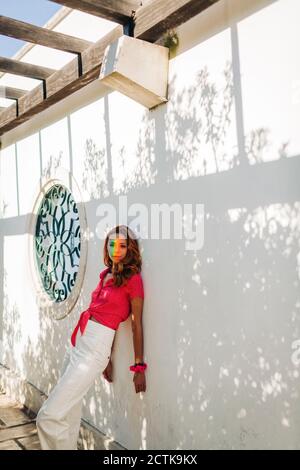 Young woman with multi colored light on face standing against wall at Alfama, Lisbon, Portugal Stock Photo