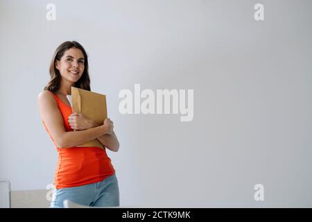 Woman holding paper in hand while standing against white wall at home Stock Photo