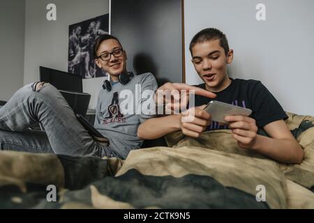 Teenage boys sitting on bed, having fun using portable devices Stock Photo