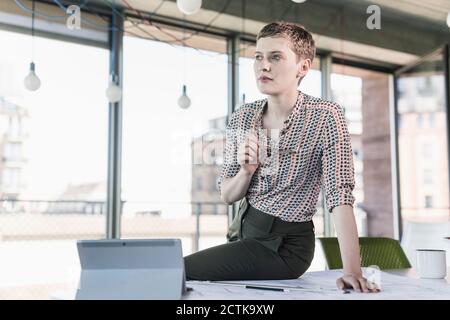 Thoughtful businesswoman sitting on desk in office Stock Photo