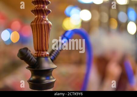 Wooden hookah close-up in the lounge bar on the background of a smoking woman. Abstract bokeh light on background. Traditional Arabian shisha. Stock Photo