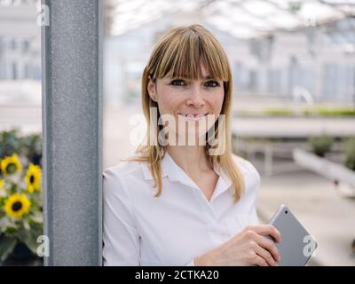 Close-up of smiling businesswoman with digital tablet standing in greenhouse Stock Photo