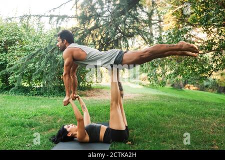 Female athlete balancing boyfriend on legs while holding hands in park Stock Photo
