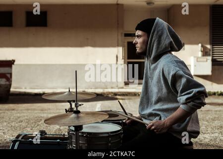 Handsome musician wearing hood playing drums at back yard Stock Photo