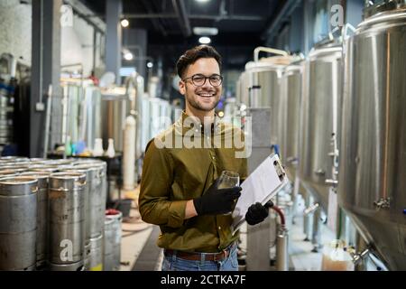 Portrait of happy man holding clipboard and beer glass in craft brewery Stock Photo