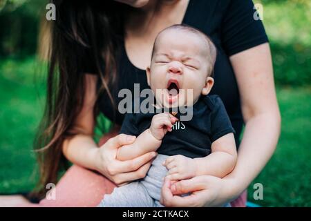 Tired baby boy yawning while sitting with mother at park during weekend Stock Photo