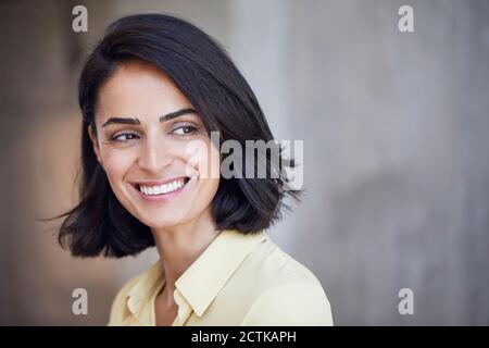 Close-up of happy businesswoman contemplating against wall in office Stock Photo