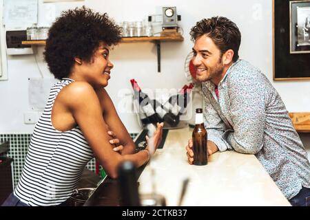 Smiling man holding beer bottle flirting with female bartender while standing at bar counter Stock Photo