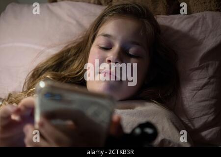 Girl using smart phone while lying in bedroom Stock Photo