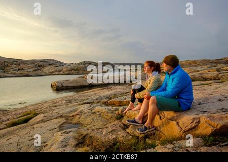 Sweden, Vastra Gotaland County, Grebbestad, Man and teenage girl sitting together on coastal rocks at Tjurpannans Nature Preserve Stock Photo
