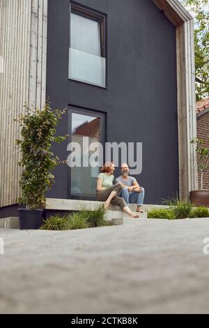 Cheerful couple sitting on steps outside tiny house Stock Photo