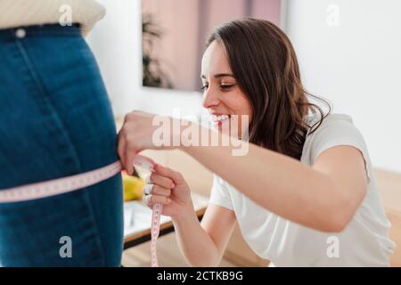 Young woman with measure tape measuring friend's thigh at home Stock Photo