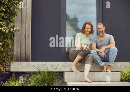 Smiling couple sitting on steps outside tiny house Stock Photo