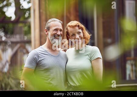 Smiling couple looking away while standing against tiny house in yard Stock Photo