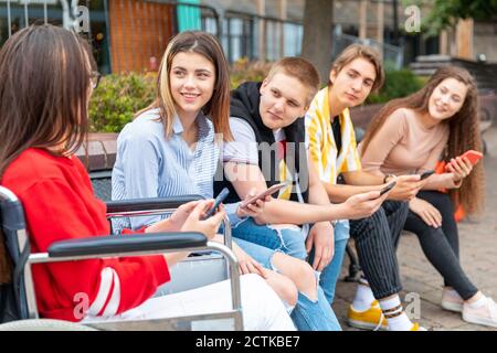 Young men and women listening to female friends while using smart phones Stock Photo