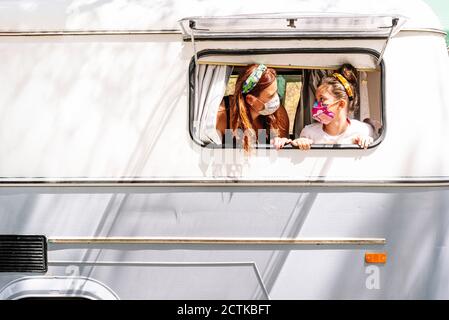 Mother and daughter wearing masks looking at each other in motor home seen through window Stock Photo