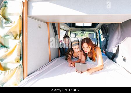 Mother with daughters using digital tablet while lying on bed in motor home Stock Photo