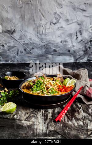 Bowl of red curry soup with rice noodles, beef, vegetables, scallion, peanuts and lime Stock Photo