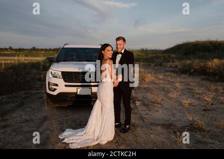 Smiling woman with male partner standing against car in field Stock Photo