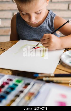 Cute boy holding paintbrush while painting on paper at home Stock Photo