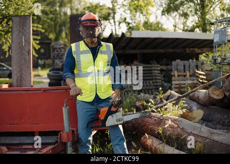 Man holding chainsaw while standing by log in forest Stock Photo