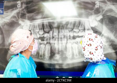 Dentist and assistant in protective workwear examining dental x-ray at office Stock Photo