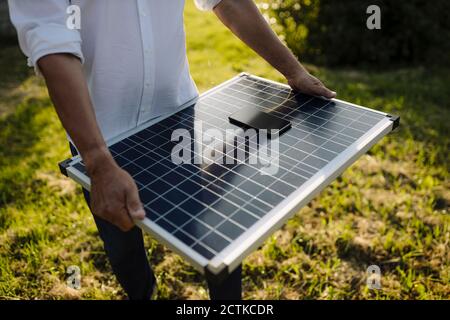 Man holding solar panel with smart phone in yard Stock Photo