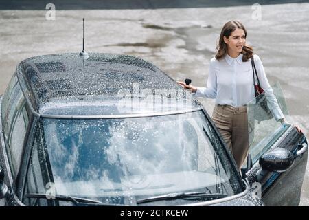 Young woman opening door of car while standing at parking lot Stock Photo